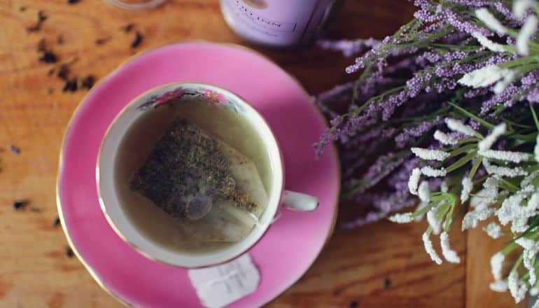 cup of lavender tea next to lavender flowers