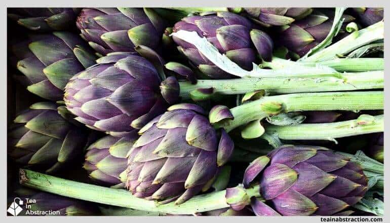 purple artichokes with green stalks in a pile