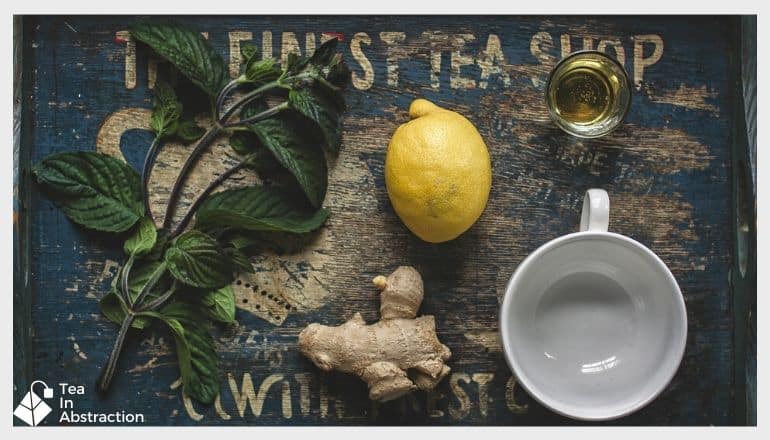 empty tea cup next to a lemon and ginger root on a table with other spices around them