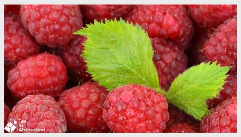 cluster of red rasperries with a green raspberry leaf in the middle