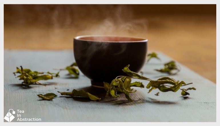 a cup of green tea sitting on a table with green tea leaves strewn about on the table