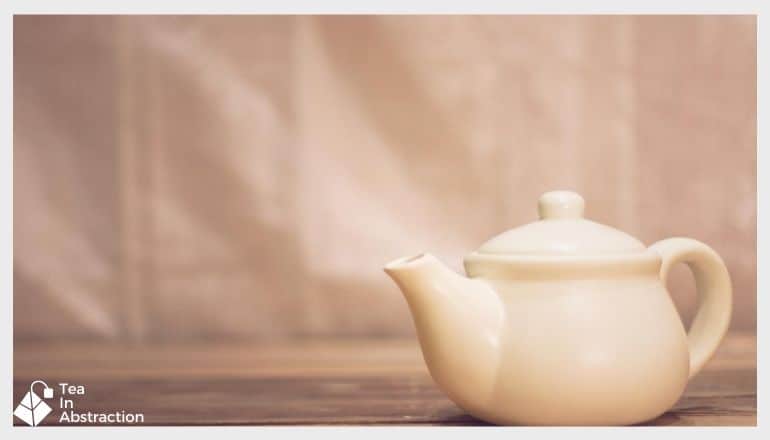 white tea kettle on a table with pomegranate green tea ready to pour